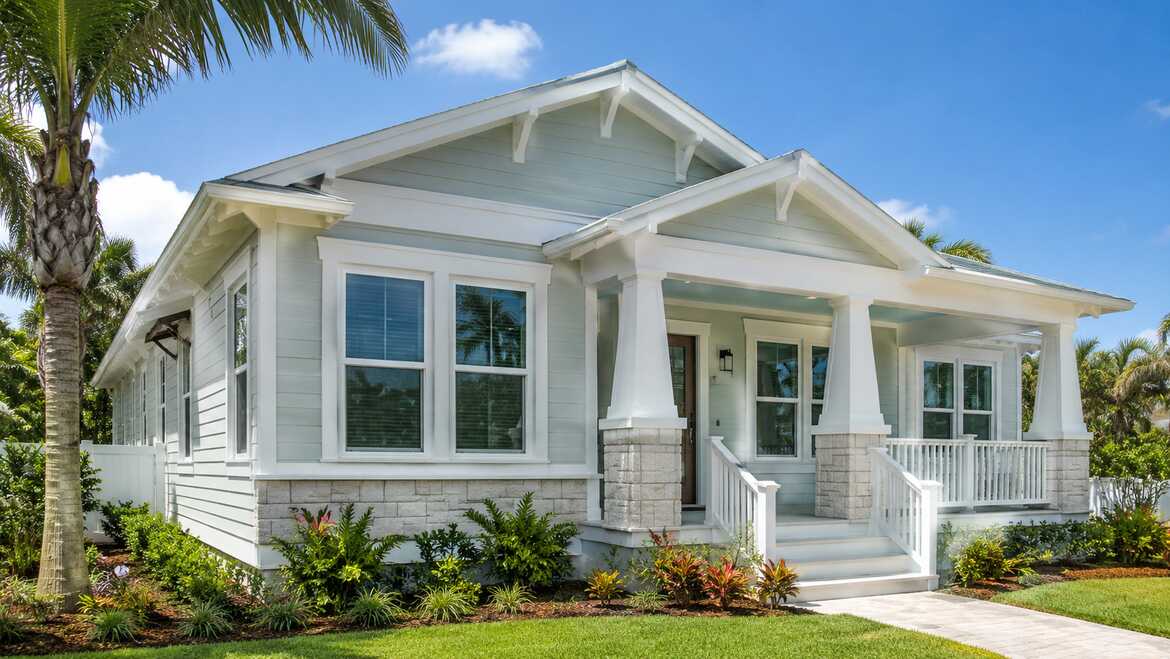 Coastal-style home exterior featuring white replacement windows, a covered porch, and tropical landscaping.